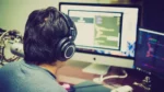 Agentic AI coding tool — real photo of a person wearing headphones working at two monitors showing code