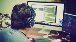 Agentic AI coding tool — real photo of a person wearing headphones working at two monitors showing code