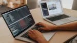AI SEO agent for small business — real photo of hands typing code on a laptop beside a second laptop