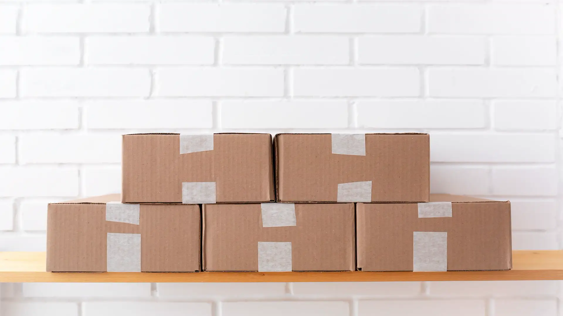 Oracle Fusion supply chain planning — real photo of stacked cardboard delivery boxes against a white brick wall