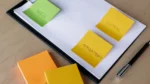 answer engine optimization checklist — Top-down view of a clipboard holding a planning sheet with colorful sticky notes labeled plan, marketing and problems, and a black pen on a wooden desk