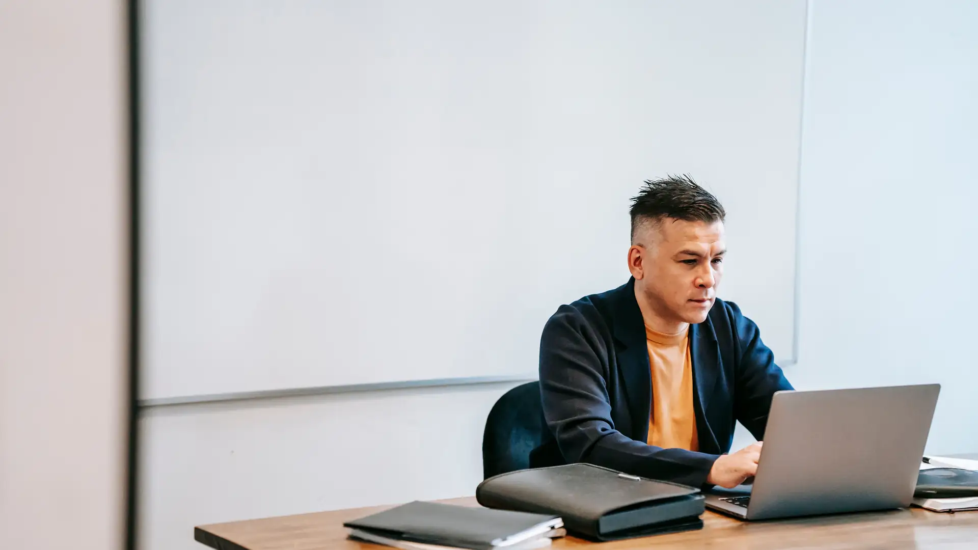 ai ad copy generator — a focused businessman typing on a laptop at an office desk in front of a whiteboard.
