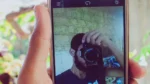 free ai avatar generator — a hand holds a white smartphone showing a selfie portrait on its camera screen.