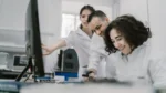 google ai research europe — three scientists in lab coats gather around a computer monitor in a bright modern laboratory.