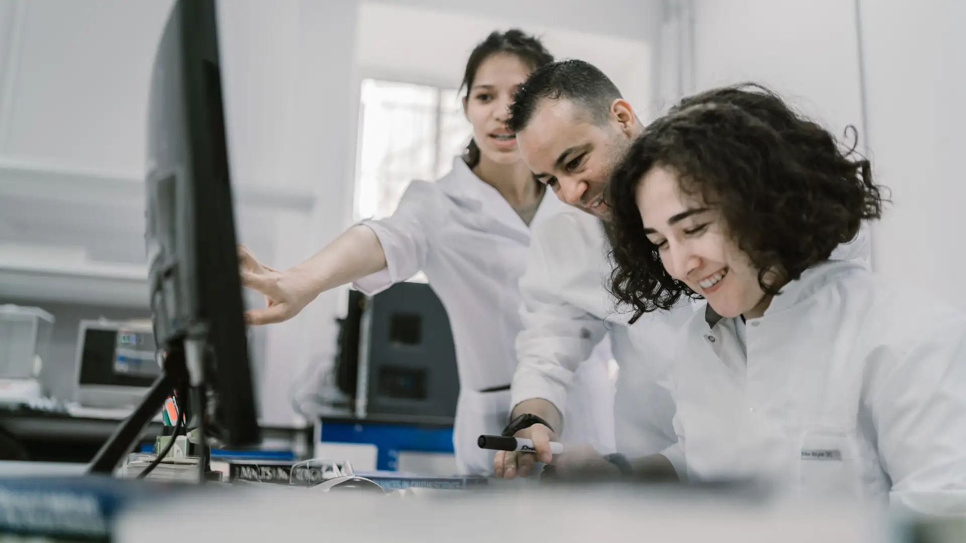 google ai research europe — three scientists in lab coats gather around a computer monitor in a bright modern laboratory.