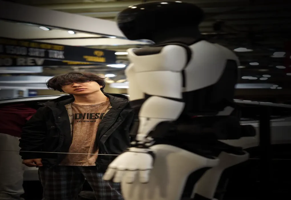 Humanoid robots shipped 2026 report — real photo of a white and black humanoid robot on display at an exhibition with a visitor beside it