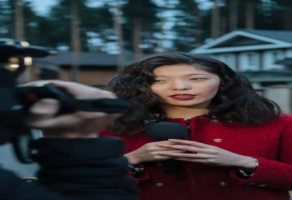 AI interview transcription software — real photo of a woman in a red coat being interviewed outdoors, holding a microphone while a camera films her