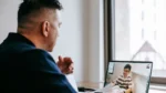ai meeting notes app — a man joins a video call on his laptop with a smiling colleague visible on the screen.