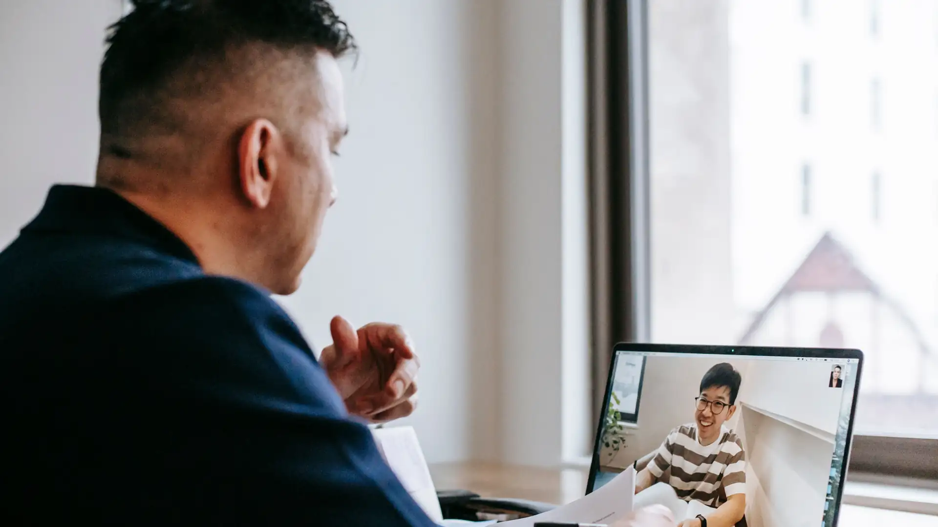 ai meeting notes app — a man joins a video call on his laptop with a smiling colleague visible on the screen.