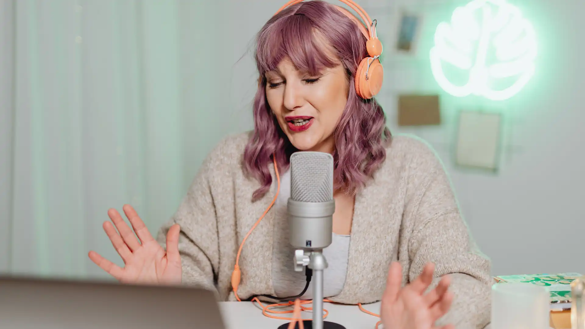 free ai noise remover — a woman with purple hair wearing orange headphones speaks into a studio microphone at her desk.