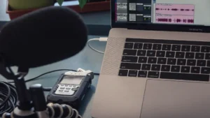 AI podcast transcript generator — real photo of a podcast recording setup with a microphone, Zoom H4n Pro recorder, and a MacBook Pro showing audio editing waveforms