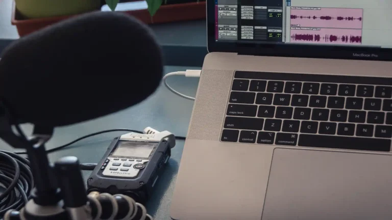 AI podcast transcript generator — real photo of a podcast recording setup with a microphone, Zoom H4n Pro recorder, and a MacBook Pro showing audio editing waveforms