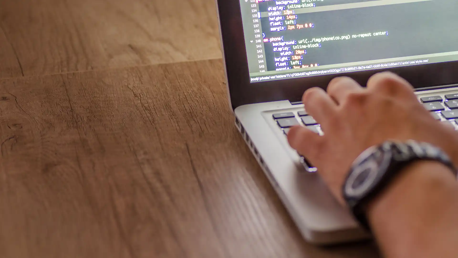 free ai sql generator — a developer's hand types on a laptop keyboard with lines of code on the screen.