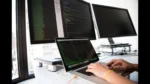 ai test case generator — a developer types on a laptop in front of multiple monitors showing code.