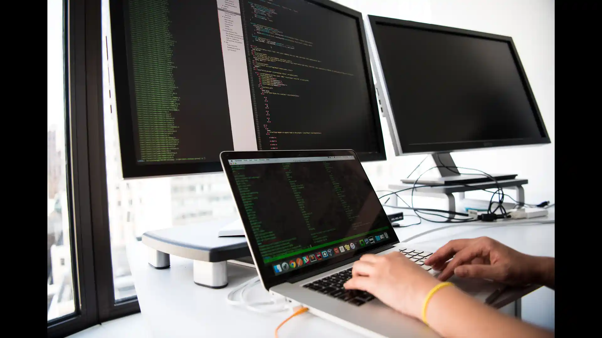 ai test case generator — a developer types on a laptop in front of multiple monitors showing code.