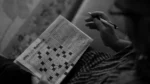 how to solve connections nyt — A person holding a pen and a newspaper crossword puzzle page, solving the black and white word puzzle grid.