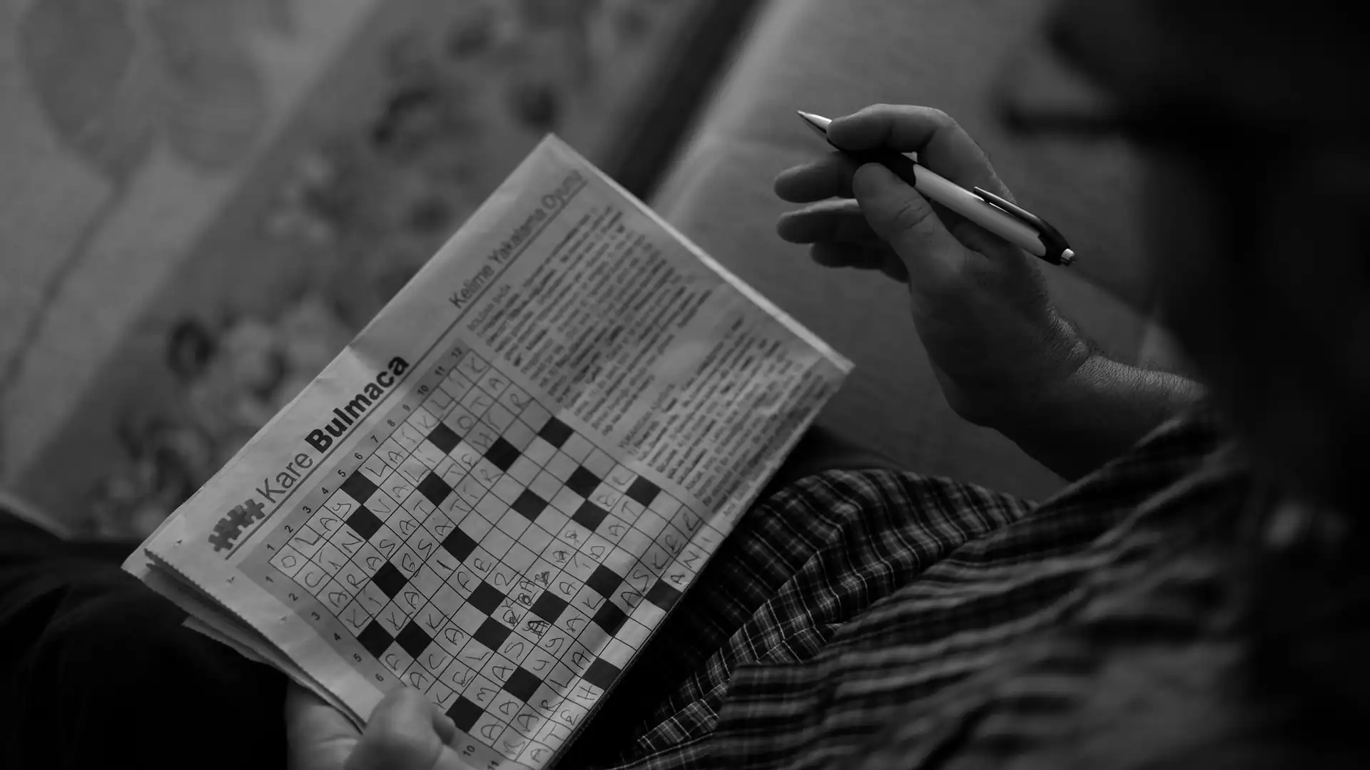 how to solve connections nyt — A person holding a pen and a newspaper crossword puzzle page, solving the black and white word puzzle grid.