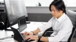 ai code explainer tool — a developer working at a desk with code on his monitor and laptop