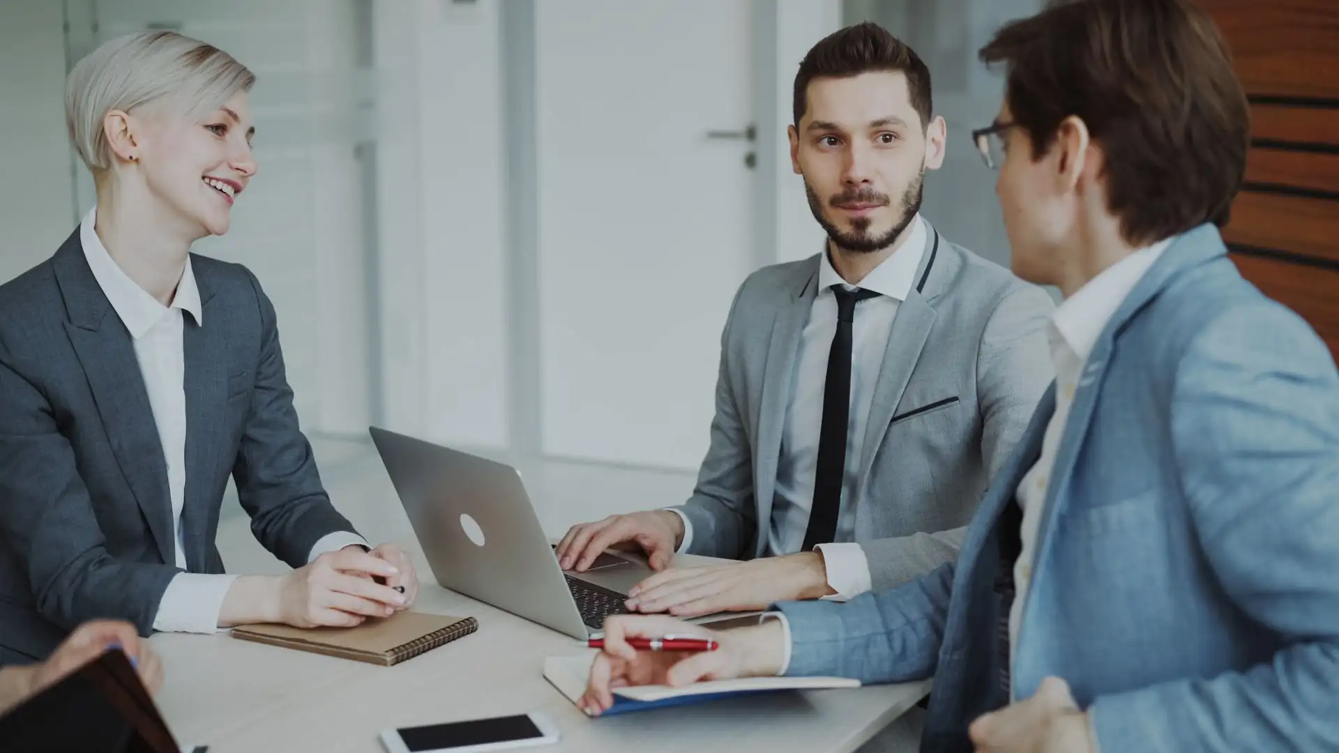 Strategic technology solutions — three business professionals discussing strategy around a table with a laptop and notebooks