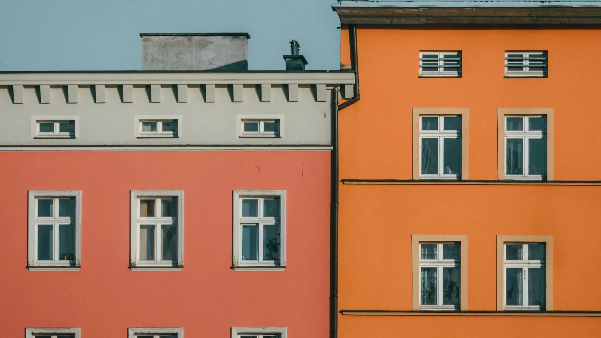 Two neighboring building facades in coral red and orange, seen side by side under a clear sky.