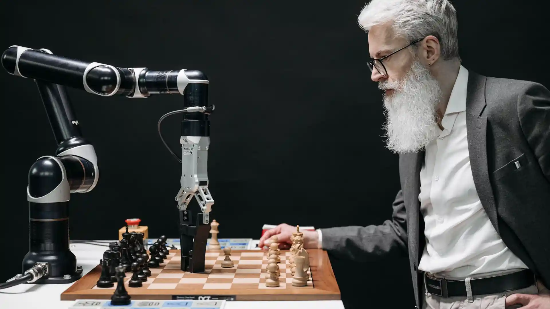 artificial intelligence versus machine learning — bearded man playing chess against a robotic arm, an example of classic AI strategy systems