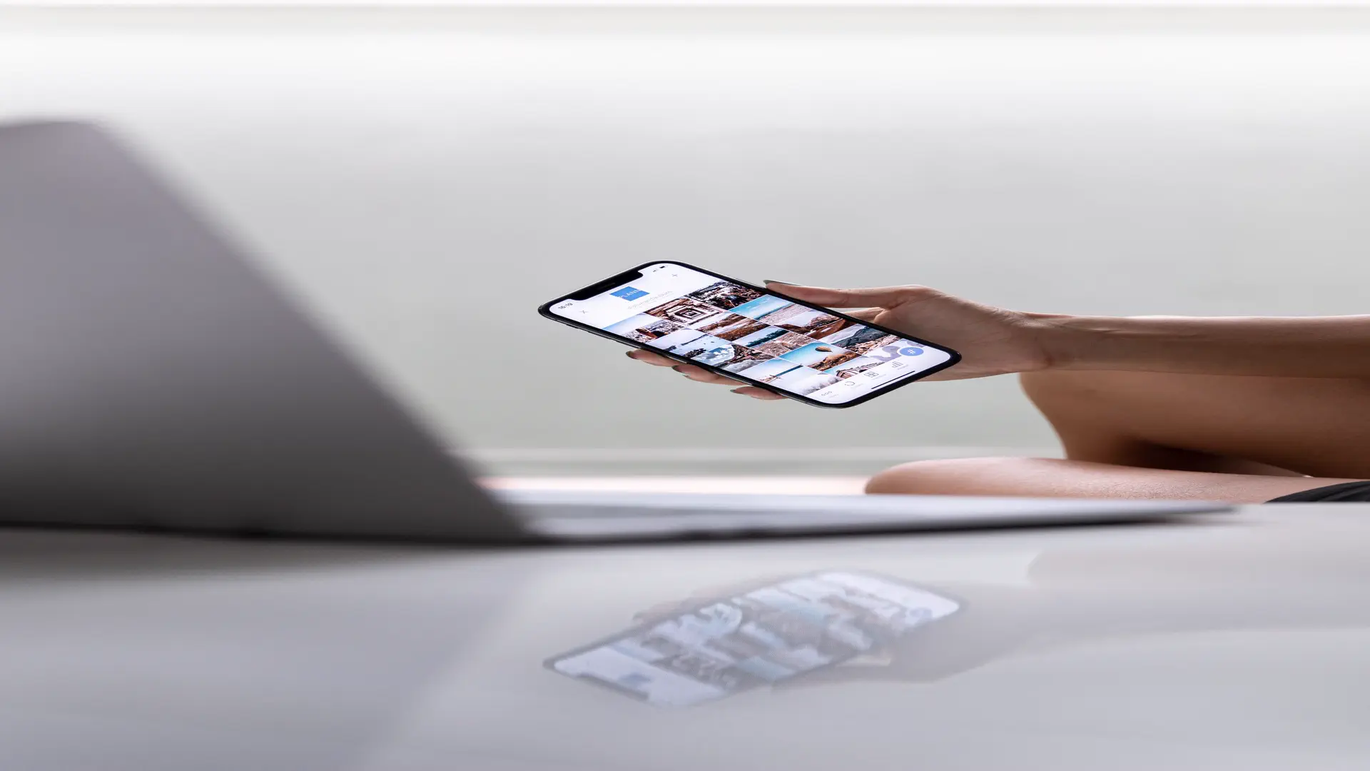 AI social media scheduling tools — real photo of a hand holding a smartphone showing a photo feed beside a laptop