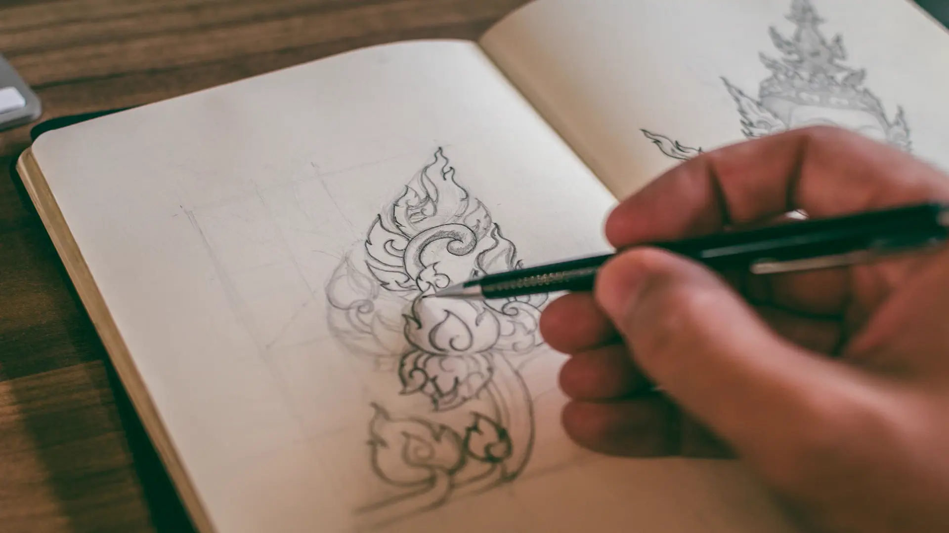 Best AI logo maker tools — real photo of a hand sketching an ornate design in a notebook